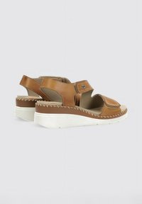 Sandalias de cuero marrón con una amplia correa en el tobillo, diseño de punta abierta y una suela de cuña blanca y contorneada con detalles de costura.
