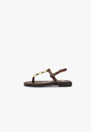 Sandalia plana marrón con adornos ovalados dorados en la tira y hebilla ajustable en el tobillo, mostrada de lado sobre fondo blanco.