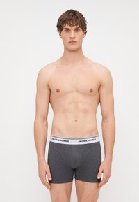 Sive bokserice s bijelim elastičnim pojasom na kojem je ispisan logo "JACK & JONES", pokazujući prilagođeni dizajn i glatku teksturu.