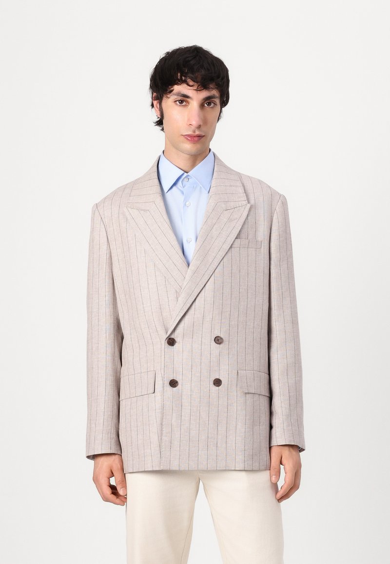 Double-breasted blazer in light beige fabric with subtle blue stripes, featuring large brown buttons and two front pockets, notched lapels.