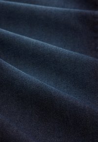 Tissu bleu foncé avec des plis doux et une surface légèrement texturée et lisse.