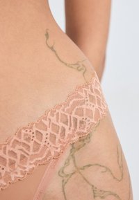Lingerie en dentelle d'un doux pêche, avec une bordure en dentelle géométrique et un tissu léger et transparent. Les détails incluent un bord brodé.