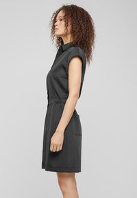 Robe noire à manches courtes avec un col, taille cintrée et poches latérales ; tissu léger au toucher doux et longueur jusqu'aux chevilles.