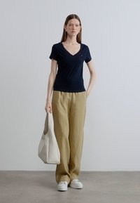 Μπλε ναυτικό T-shirt με V λαιμόκοψη, μπεζ λινά παντελόνια, άσπρα αθλητικά παπούτσια και κρεμ τσάντα. Απλός σχεδιασμός, χαλαρή εφαρμογή και απαλές υφές.