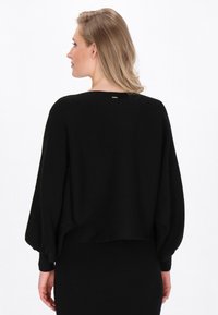 Schwarzer, verkürzter Pullover mit übergroßen Ärmeln, geripptem Muster und Rundhalsausschnitt. Verfügt über ein kleines metallisches Detail am Rücken.