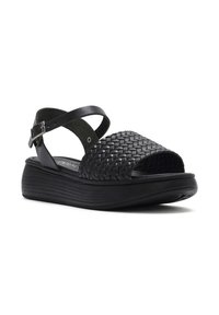 Sandal in pelle intrecciata nera con punta aperta, cinturino alla caviglia regolabile e suola piatta imbottita. Superficie testurizzata con vestibilità sagomata.