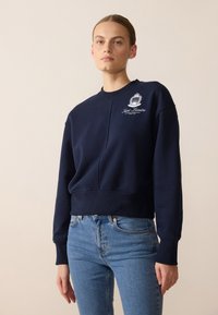 Felpa blu navy con girocollo, polsini a coste e design cropped. Presenta un logo grafico bianco sul lato sinistro del petto.