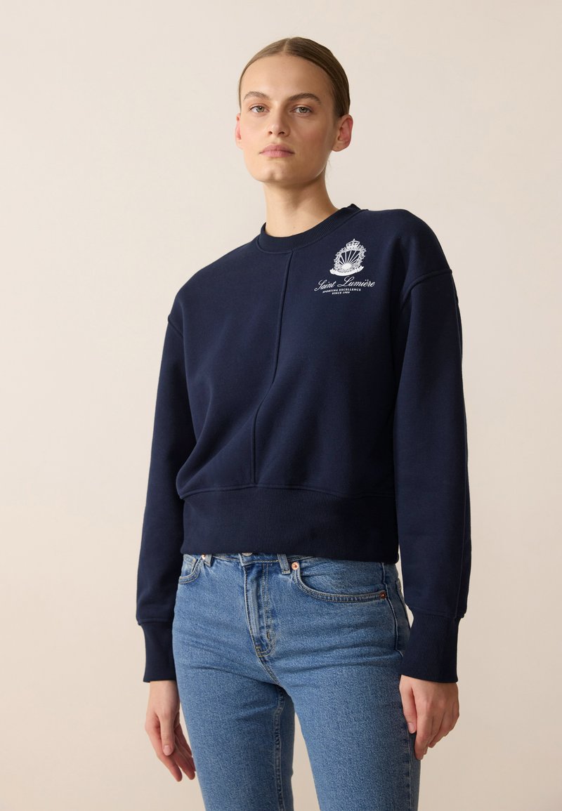 Felpa blu navy con girocollo, polsini a coste e design cropped. Presenta un logo grafico bianco sul lato sinistro del petto.