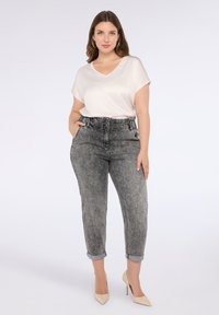 Top bej deschis cu decolteu în V și mâneci scurte, asortat cu blugi gri cu talie înaltă, având o textură estompată și manșete răsucite. Pantofi cu toc bej completează ținuta.
