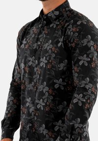 Maglietta nera a maniche lunghe con motivo floreale di fiori grigi e arancioni, realizzata in tessuto liscio, con chiusura a bottoni sul davanti e colletto.