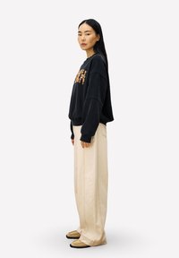 Zwarte oversized sweatshirt met getextureerde lettering, beige wijdvallende broek en donkere instap schoenen. Minimalistisch ontwerp met een ontspannen pasvorm.