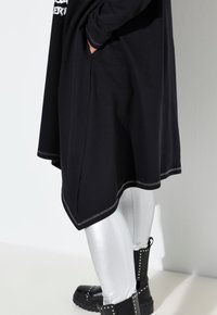 Zwarte tuniek met een loose fit, hoge-lage zoom en zilveren stiksels, gecombineerd met glanzende zilveren leggings en zwarte enkelboots met studs.