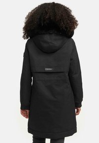 Black long coat with a fur-trimmed hood, cinched cuffs, and a horizontal seam detail. Features a visible brand label on the back.