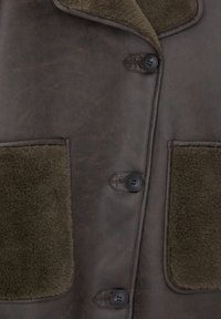 Chaqueta de piel sintética marrón con un cuello de piel sintética verde y grandes bolsillos frontales, con botones negros y una textura suave.