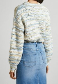 Pull en maille crème et bleu, présentant un design texturé et à motifs avec des manches ballon. Associé à une jupe en denim clair avec poches.