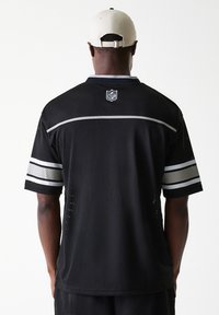 Maillot NFL noir en tissu à mailles, avec des manches courtes et des rayures argentées, et un logo dans le dos au niveau du col. Détails texturés tout au long.
