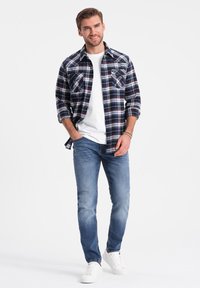 Camicia di flanella a quadri nei colori blu navy, rosso e bianco sopra una t-shirt bianca; abbinata a jeans azzurri chiari e sneakers bianche. Look casual.