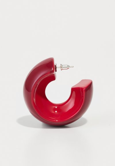 Rote Polymer-Hoop-Ohrstecker mit glänzender Oberfläche, die ein geschwungenes Design aufweisen und mit einem silbernen Verschluss ausgestattet sind. Glatte Textur mit markantem Format.