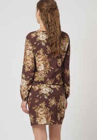 Vestido floral marrón con mangas largas, que presenta una tela texturizada y una cintura entallada. Grandes patrones de flores beige y verdes por toda la prenda.