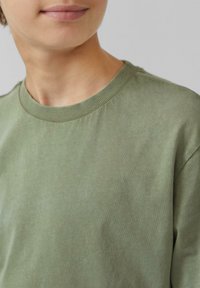 Olijfgroene katoenen T-shirt met een ronde hals, ribbelhals en korte mouwen; gladde textuur met subtiele kleurvariaties.