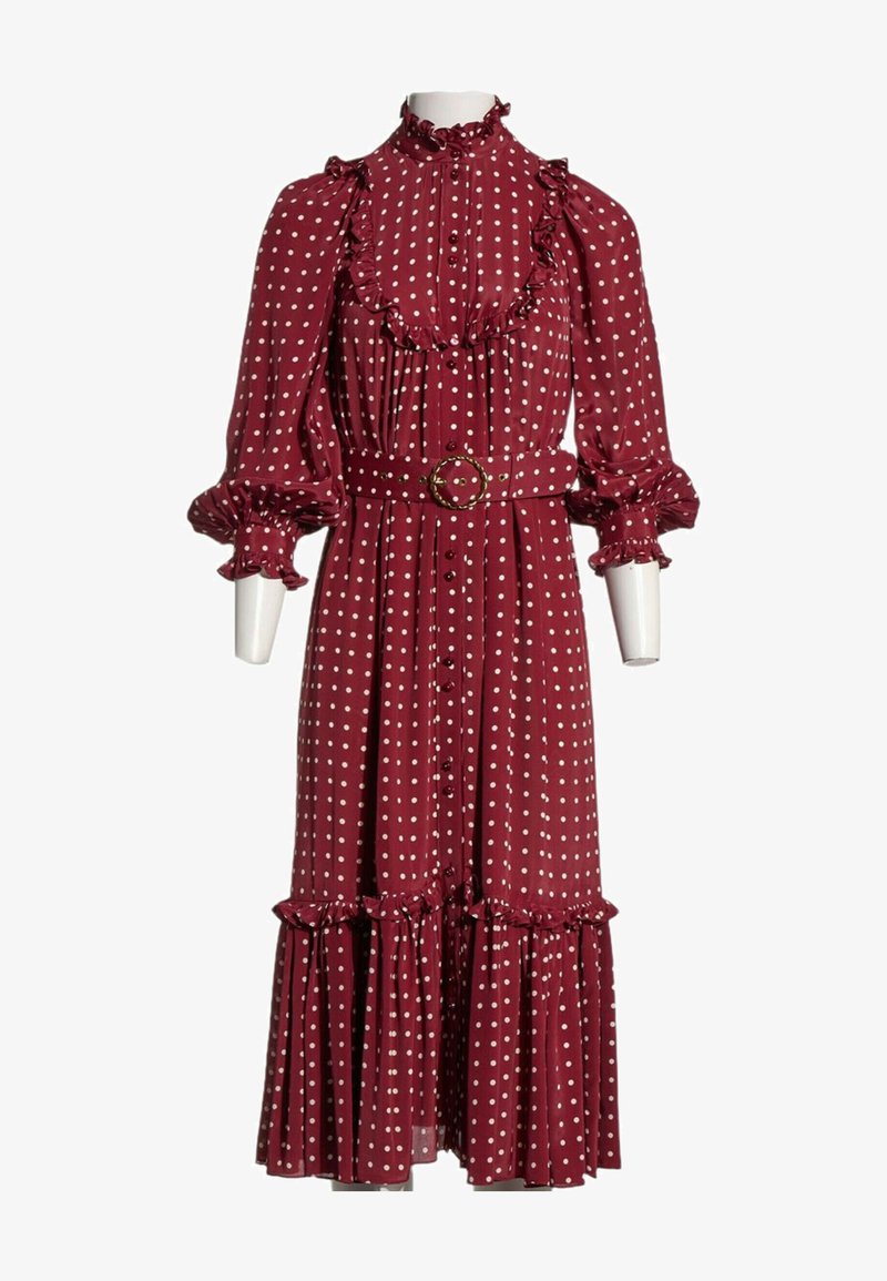Robe longue bordeaux à pois blancs, col montant à volants, manches longues bouffantes, boutonnée devant et taille ceinturée avec une boucle circulaire.