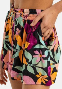 Shorts fleuris avec un fond noir, présentant des couleurs vives comme le rose, l'orange et le vert. Tissu léger, texturé avec une finition froissée.