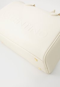 White pebbled leather handbag with embossed "VALENTINO" logo, gold-tone hardware, rounded edges, and four metal feet for stability.