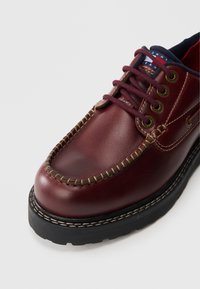 Burgunderfarbene Lederschuhe mit runder Zehenform, kontrastierenden Nähten und Metallösen. Ausgestattet mit einer strukturierten schwarzen Gummisohle.