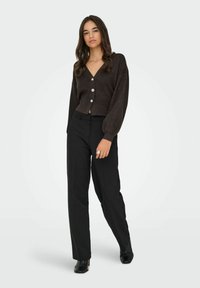 Brown knitted cardigan with a V-neck, five decorative buttons, and puff sleeves, paired with high-waisted black trousers and heeled black boots.