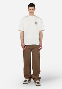 Tricou oversized din bumbac alb, cu guler rotund și logo pe piept. Asortat cu pantaloni largi maro și teniși albi cu accente maro.