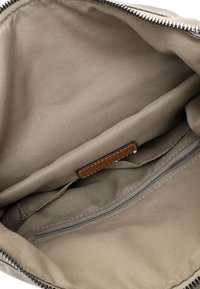 Interno di una borsa in tessuto grigio con una tasca con zip e un'etichetta in pelle marrone. Texture liscia e cuciture pulite lungo i bordi.