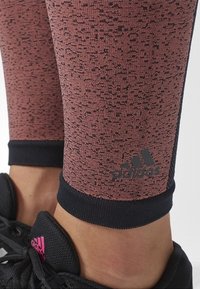 Mallas en color malva texturizado con motas negras, con un puño negro y un pequeño logo negro. Combinadas con zapatillas deportivas negras.