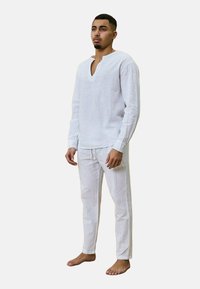 Ensemble en lin blanc composé d'une tunique à manches longues avec un col en V et d'un pantalon à cordon, présentant un tissu texturé et une coupe décontractée.