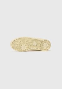 Sneaker outsole in beige rubber with herringbone pattern, circular accents, and textured surface for grip. Flat and slightly raised design.