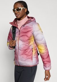 Μπουφάν σε μετάβαση ροζ, μωβ και κίτρινου με σχεδίαση καπιτονέ. Διαθέτει κλείσιμο με φερμουάρ και κουκούλα, φορεμένο με ροζ στρώμα εσωτερικά.