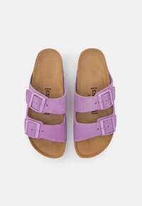 Purple suede slide sandals with two adjustable buckles, featuring a textured brown footbed and open-toe design.