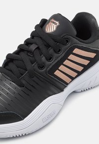 Scarpa da atletica nera con superficie testurizzata, accenti in mesh e strisce in rosè dorato. La suola è bianca con un motivo rigato per migliorare la trazione.