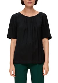 Zwarte short-sleeve top van soepel materiaal met een ronde halslijn, voorzien van subtiele plooien en een gegolfde afwerking. Gepaard met groene broek.