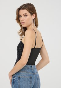 Body nero con pois bianchi, spalline sottili regolabili e un design aderente, abbinato a jeans denim sfilacciati a vita alta.