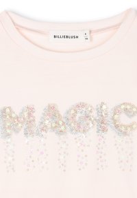 Lichtroze t-shirt met "MAGIC" in zilver en iriserende glitter, met een ronde hals en korte mouwen. Sprankelende accenten onder de tekst.