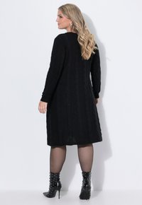Vestito nero in maglia caratterizzato da un motivo a trecce, maniche lunghe e orlo a media lunghezza. Abbinato a stivaletti neri con borchie.