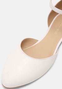 Zapato de tacón alto de cuero blanco con punta afilada y correa en el tobillo, que presenta una textura suave y detalles de costura mínimos.