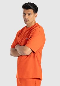 Oranžové bavlněné tričko s volným střihem, krátkými rukávy a kulatým výstřihem. Na hrudi se nachází malé logo.