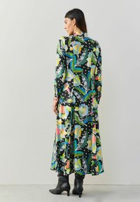 Dlouhé černé šaty s barevnými květinovými a listovými vzory, bílými puntíky a volným střihem. Doplněné černými kozačkami po kolena.