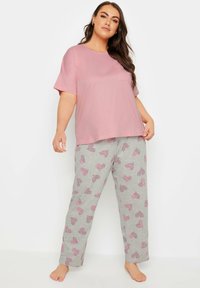 Rosa t-shirt med kort ärm med en ficka, kombinerad med ljusgrå byxor med ett hjärt- och randigt mönster i rosa. Mjuk tyg, avslappnad passform.