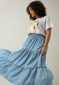 Falda maxi acampanada de color azul claro en tejido suave, con cintura elástica y cordón. Combinada con una camiseta gráfica blanca con detalles en dorado.