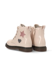 Botines de charol beige con apliques de estrellas y corazones en rosa y plata. Punta redonda, parte delantera con cordones y cremallera en la parte posterior. Suela de goma marrón.