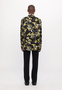 Camicia a maniche lunghe con una base nera e un motivo floreale giallo e bianco. Abbinata a pantaloni neri e scarpe nere con suola spessa.