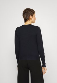 Pull en tricot bleu marine à manches longues avec des poignets et un ourlet côtes. Design simple, texture légère, détails de couture visibles.