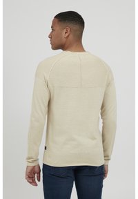 Lys beige langermet genser med ribbestruktur og sømløs bakdesign, med buet kant og kontrasterende søm.